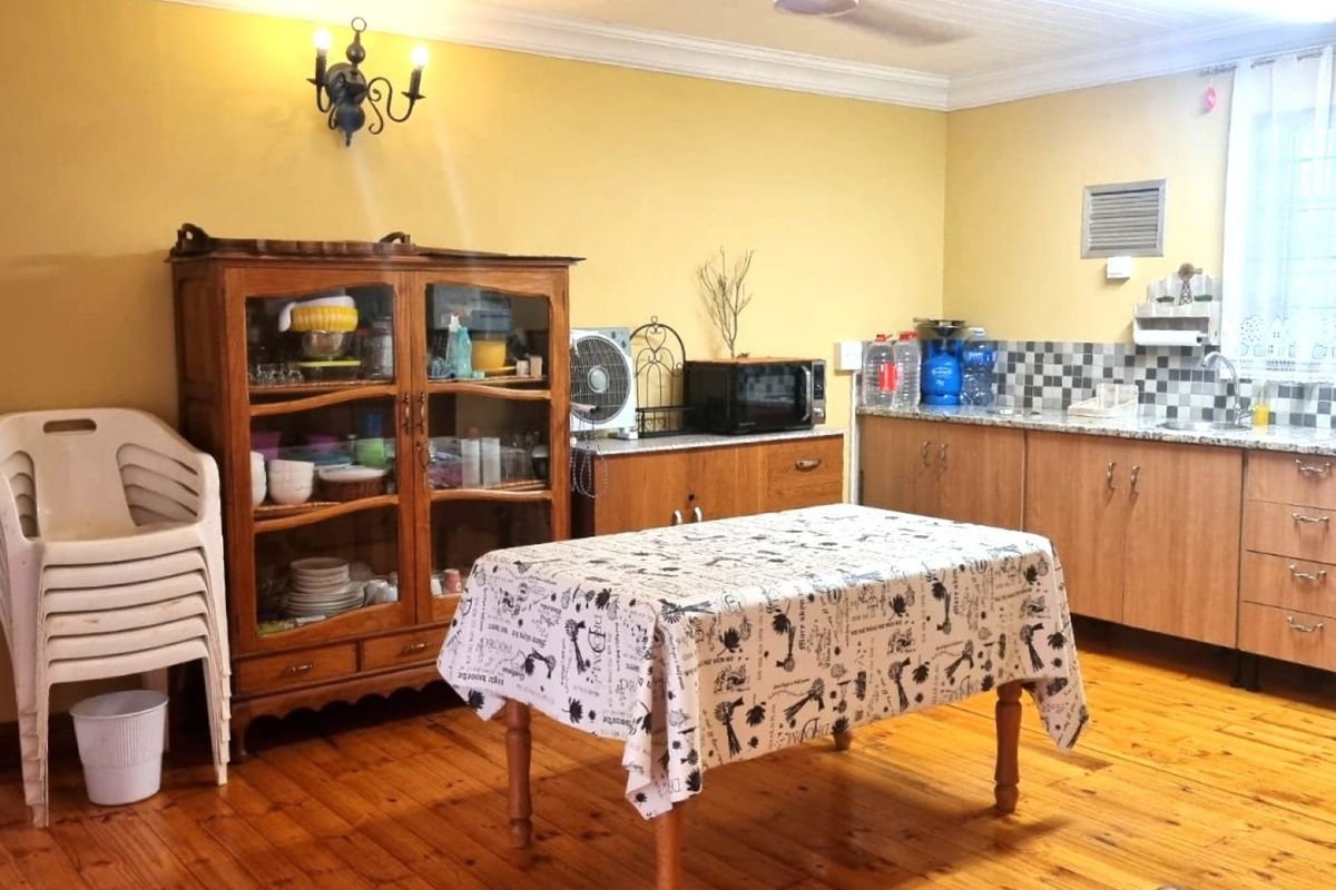 A functional kitchen featuring timber flooring, wooden cabinetry, tiled backsplash, and a stainless steel sink, offering a traditional and practical workspace.