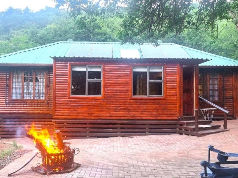 A charming log cabin exterior featuring a metal roof with integrated solar panels and a paved patio area.