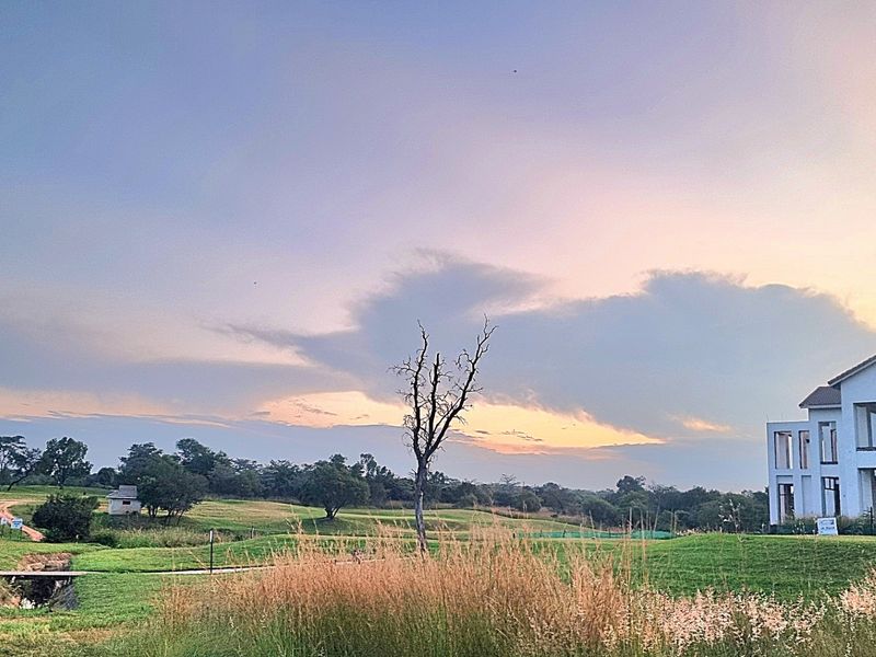 A scenic view of a residential property featuring a large building structure set within expansive, well-maintained green grounds at sunset.