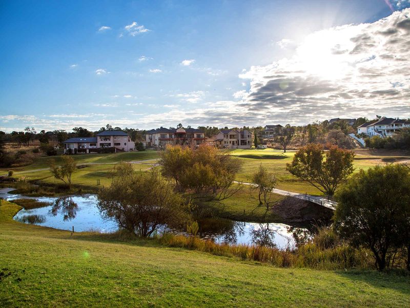 Scenic view of a well-maintained golf course estate featuring a tranquil water feature and pedestrian bridge.