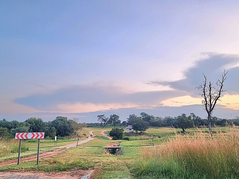 A scenic view of expansive vacant residential land featuring natural grassland, a dirt access road, and a small culvert at sunset.