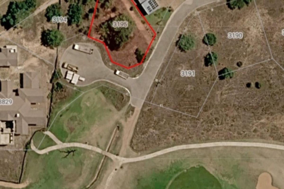 An aerial view of a vacant residential plot marked with boundary lines, situated within a developed estate near a golf course.