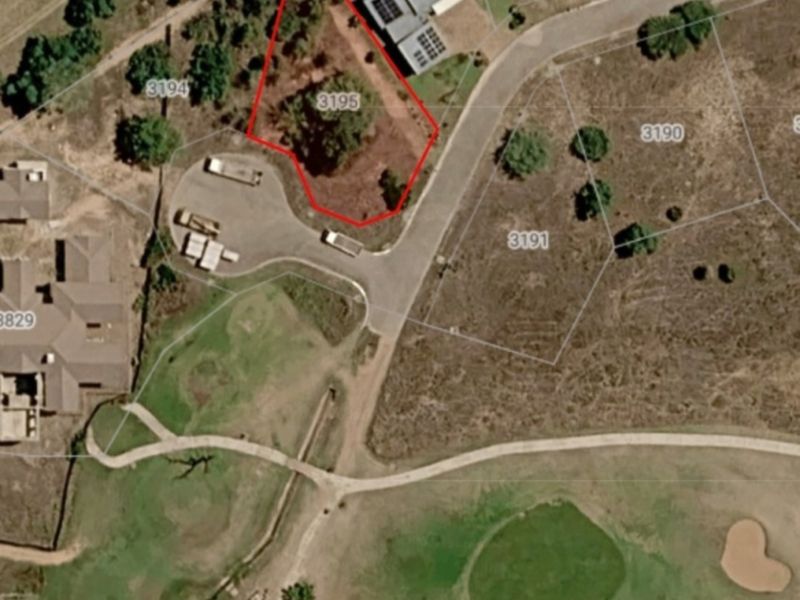 An aerial view of a vacant residential plot marked with boundary lines, situated within a developed estate near a golf course.