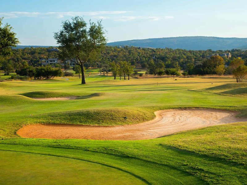A scenic view of a well-maintained golf course featuring rolling green fairways, sand bunkers, and distant mountain landscape.