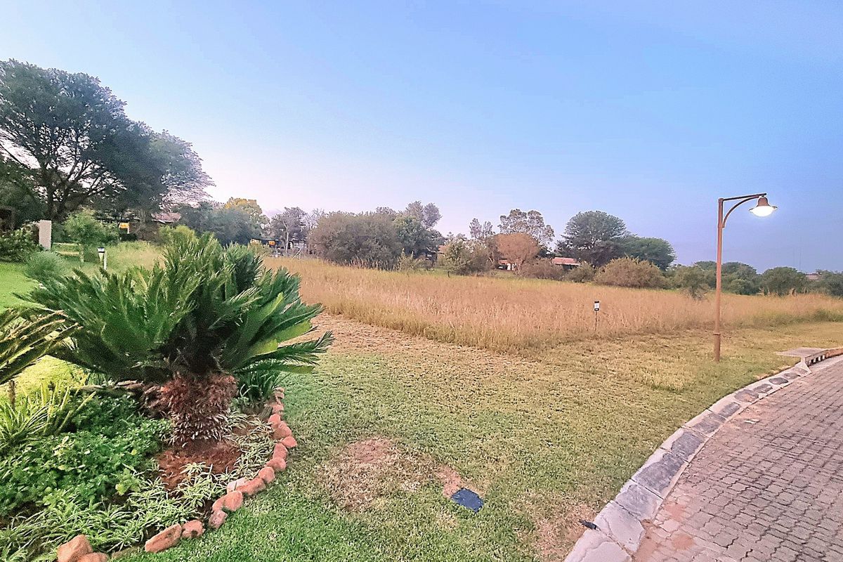 A view of a vacant residential plot featuring established landscaping, paved street access, and integrated street lighting.