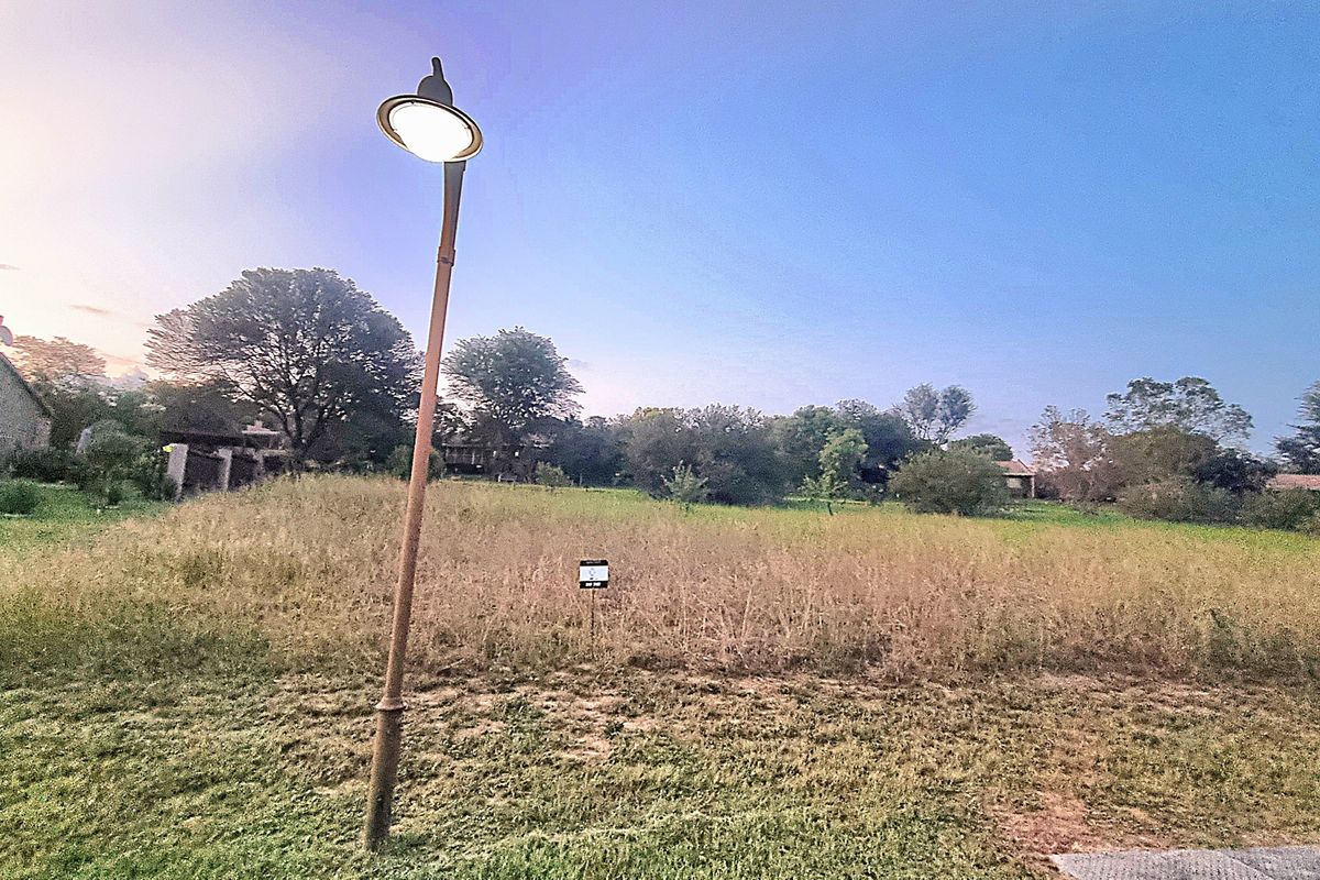 A vacant residential plot of land featuring natural grass coverage and a street lamp, situated in a residential neighborhood.