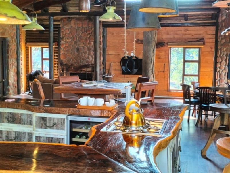 Spacious open-plan lodge interior featuring a unique live-edge timber kitchen island, stone feature walls, and rustic exposed log beam ceilings.