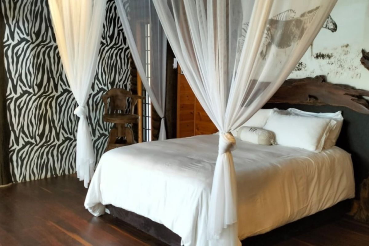 A rustic lodge bedroom featuring timber wall paneling, polished timber flooring, and a canopy bed frame with decorative wall accents.