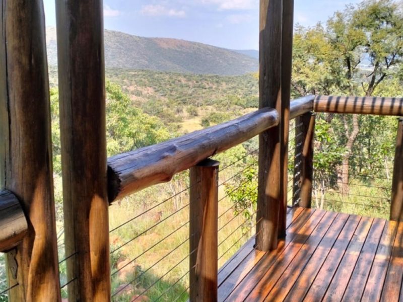 An elevated timber deck balcony featuring rustic log posts and wire balustrading, offering expansive views of the surrounding natural landscape.
