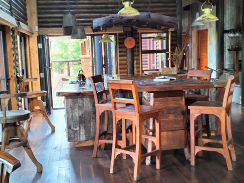 Rustic open-plan living and kitchen area featuring exposed log walls, timber flooring, and a central wooden island with integrated seating.