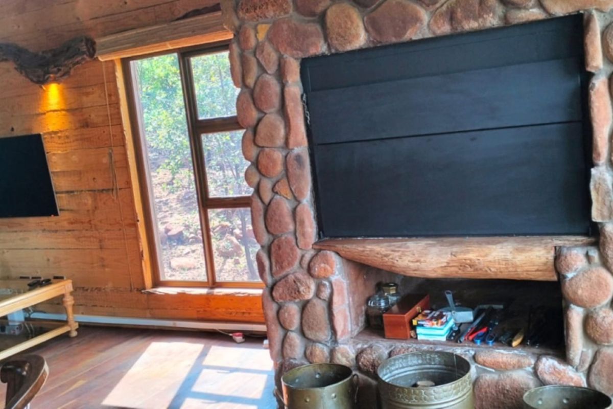 Rustic living room featuring natural timber wall cladding, hardwood flooring, and a prominent stone fireplace with a built-in hearth.