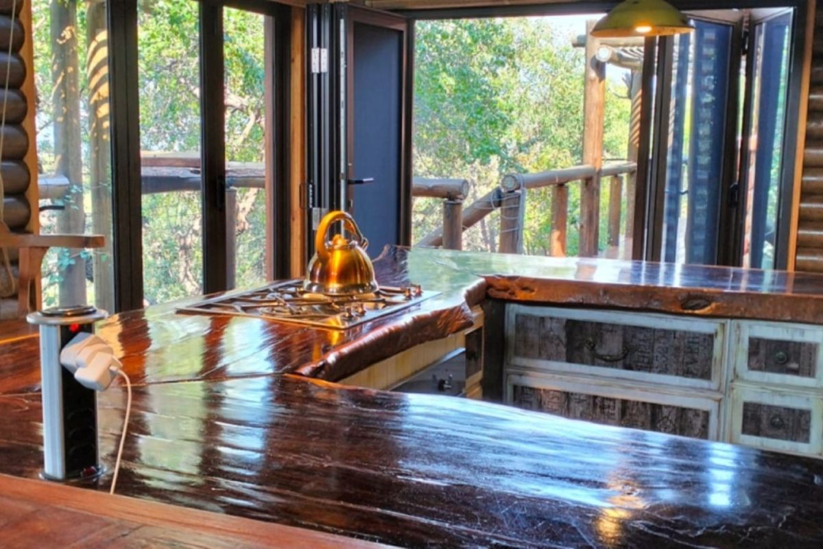 A rustic kitchen featuring a unique live-edge timber countertop, built-in gas hob, and bi-fold doors opening to a scenic outdoor deck.