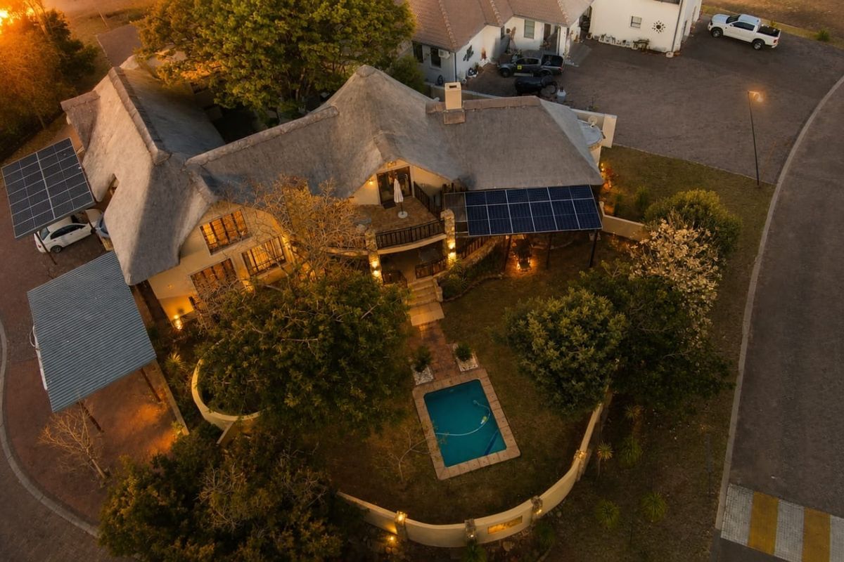 Aerial view of a residential property featuring a thatched roof, solar panel installation, private swimming pool, and landscaped garden area at dusk.