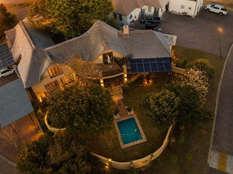 Aerial view of a residential property featuring a thatched roof, solar panel installation, private swimming pool, and landscaped garden area at dusk.