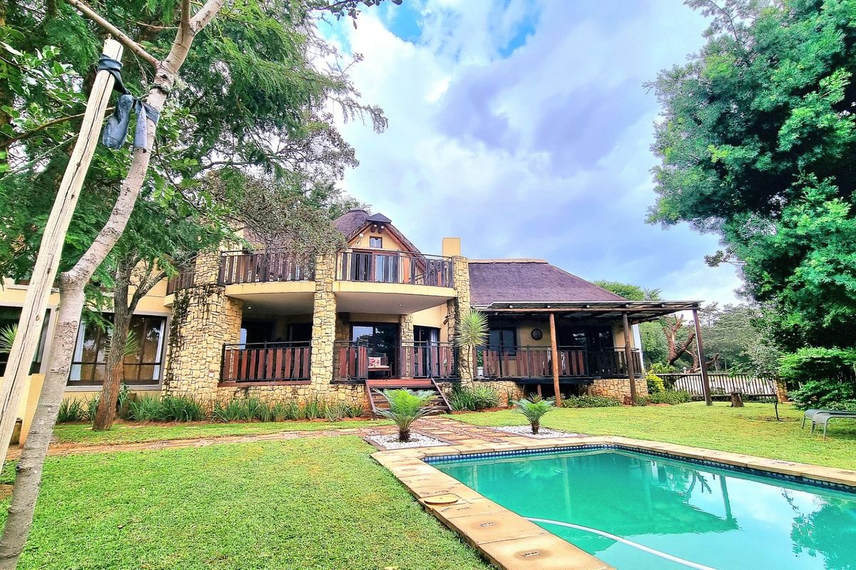 Rear view of a multi-level house featuring a swimming pool, stone-clad exterior, thatched roof, and spacious timber balconies overlooking the garden.