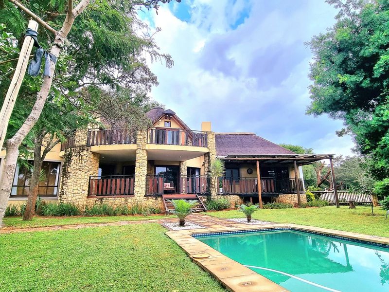 Rear view of a multi-level house featuring a swimming pool, stone-clad exterior, thatched roof, and spacious timber balconies overlooking the garden.