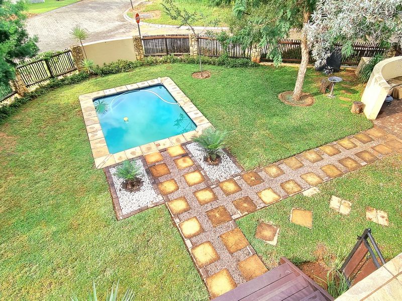 An elevated view of a private backyard featuring a swimming pool, stone-paved pathways, a built-in curved bench, and a fire pit area.