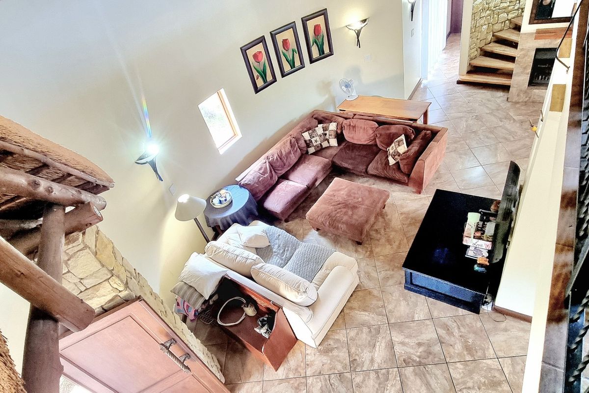 Spacious living area featuring tiled floors, a stone accent wall, and a unique thatched roof ceiling, viewed from an elevated mezzanine level.