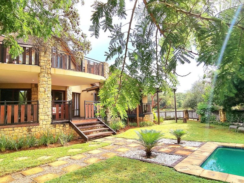 Rear view of the property featuring stone-clad exterior, multi-level balconies, timber decking, and a landscaped garden with a swimming pool.