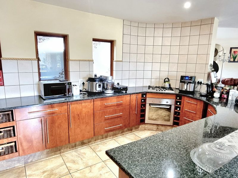 A functional kitchen featuring wooden cabinetry, granite countertops, a built-in oven, gas hob, and tiled backsplash with a curved wall design.