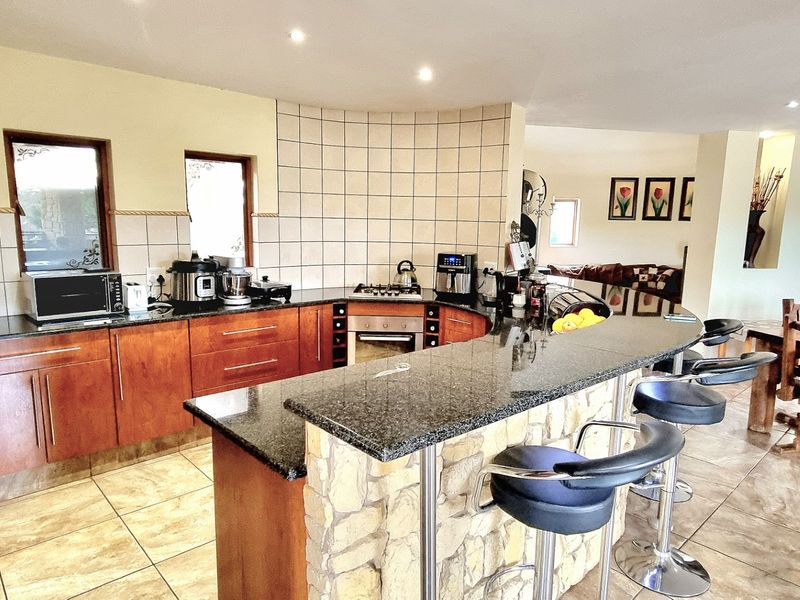Open-plan kitchen featuring a curved stone-clad breakfast bar, granite countertops, built-in oven, and gas hob, seamlessly flowing into the adjacent dining area.