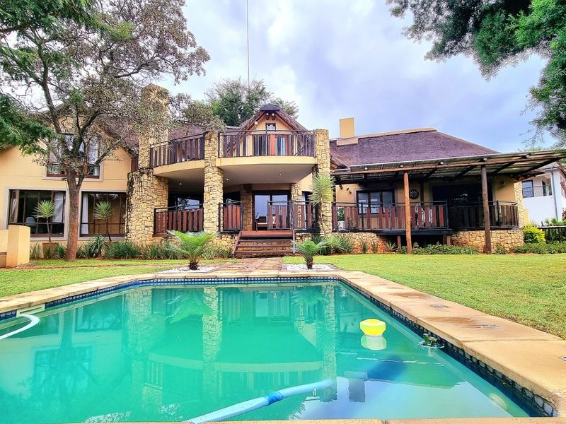 Rear view of a multi-level home featuring a swimming pool, thatched roof, stone facade, and spacious timber decking with covered patio areas.