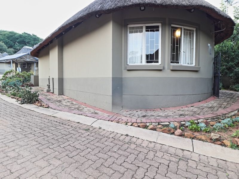 Exterior view of a house featuring a distinctive curved wall, thatched roof, and paved driveway with established garden borders.