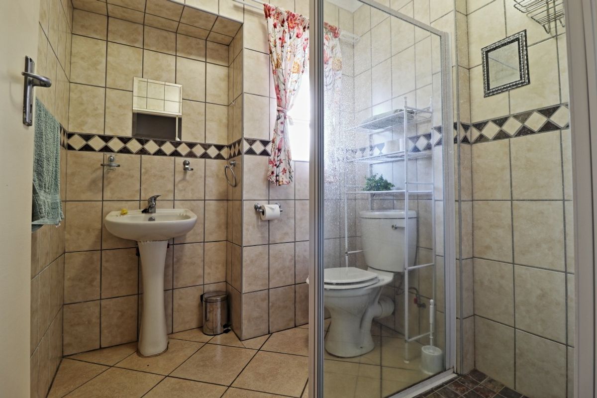 A functional bathroom featuring a pedestal basin, toilet, and a glass-enclosed shower, finished with neutral ceramic wall and floor tiling.