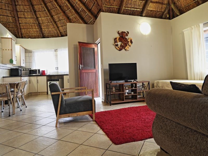 Open-plan living area featuring a distinctive thatched roof, tiled flooring, and an integrated kitchen space with functional cabinetry.