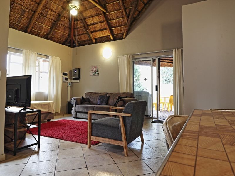 Spacious living area featuring a high vaulted thatched ceiling with exposed timber rafters, ceramic tiled flooring, and direct access to an outdoor patio.
