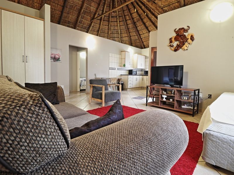 Open-plan living area featuring a traditional thatched roof, tiled flooring, and a compact kitchen with built-in cabinetry.