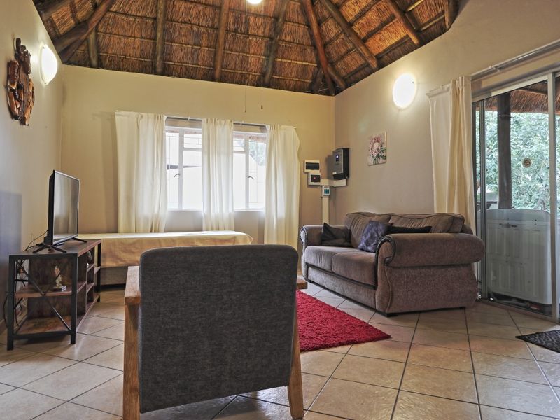 A living room featuring a high thatched ceiling with exposed timber rafters, ceramic tiled flooring, and sliding glass doors leading to an outdoor area.