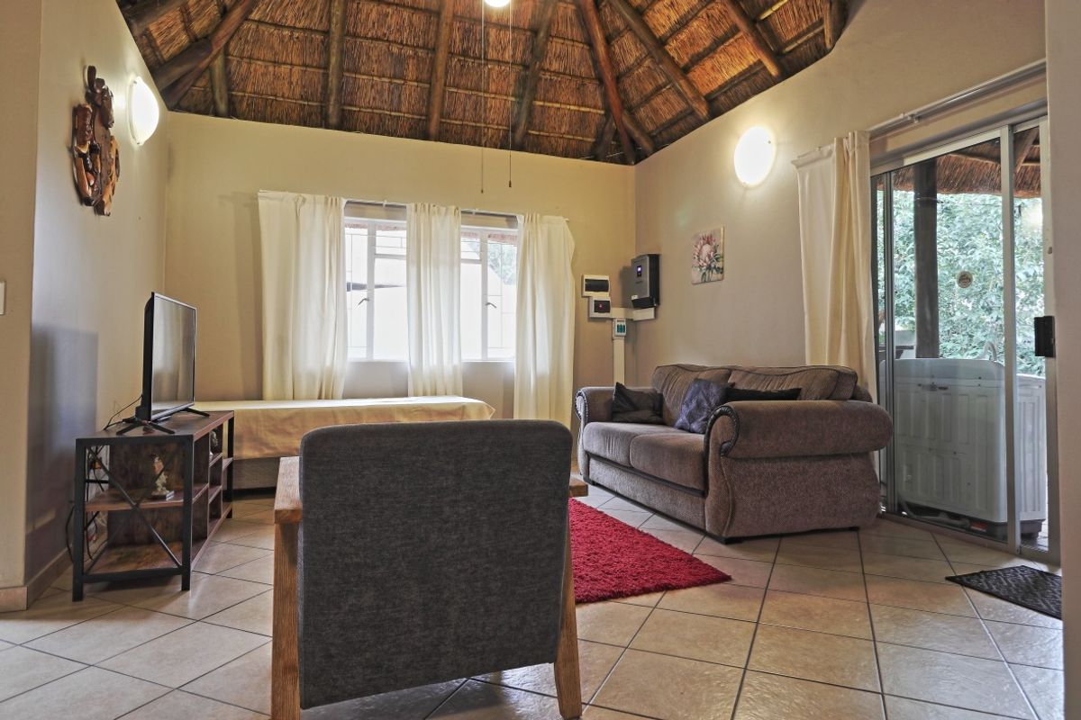 A living room featuring a high thatched ceiling with exposed timber rafters, ceramic tiled flooring, and sliding glass doors leading to an outdoor area.