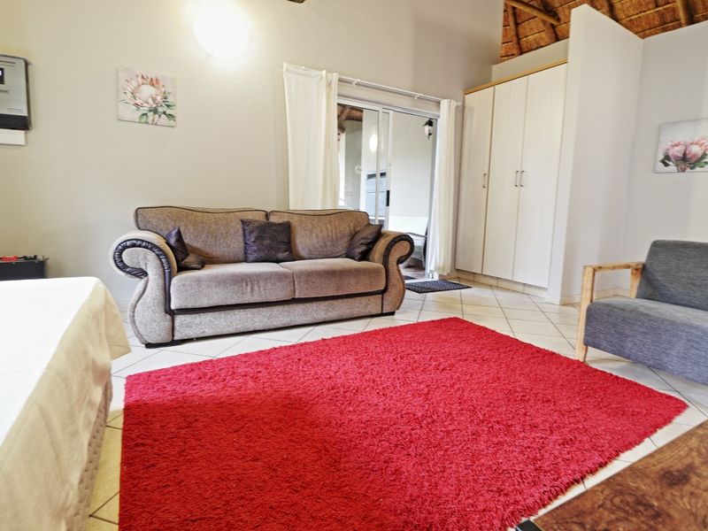A living room featuring tiled floors, built-in storage cupboards, a solar inverter, and a high thatch roof, with access to an outdoor area.