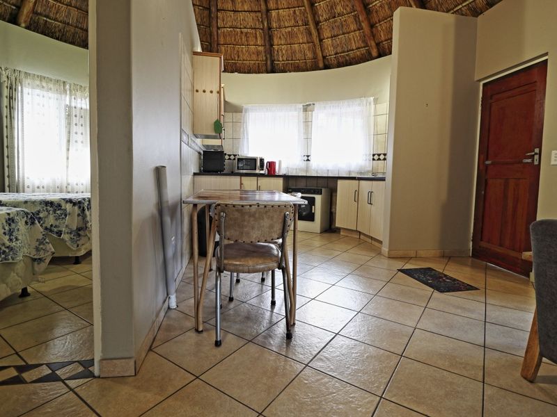 Open-plan living area featuring a traditional thatched roof, tiled flooring, and a functional kitchen space with built-in cabinetry and oven.