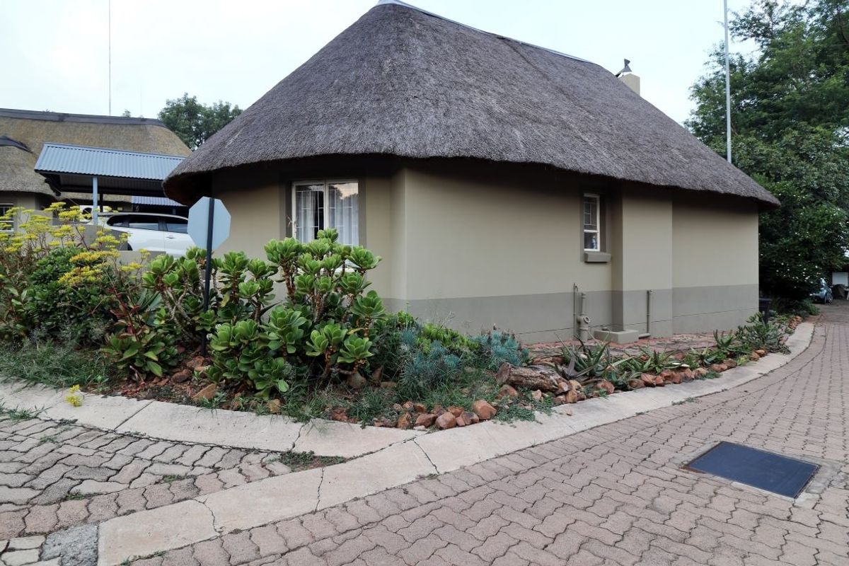 A well-maintained cottage featuring a traditional thatch roof, set within a landscaped garden with paved driveway access.