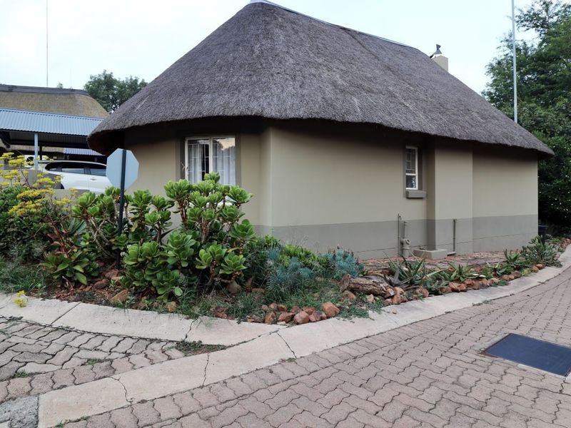 A well-maintained cottage featuring a traditional thatch roof, set within a landscaped garden with paved driveway access.