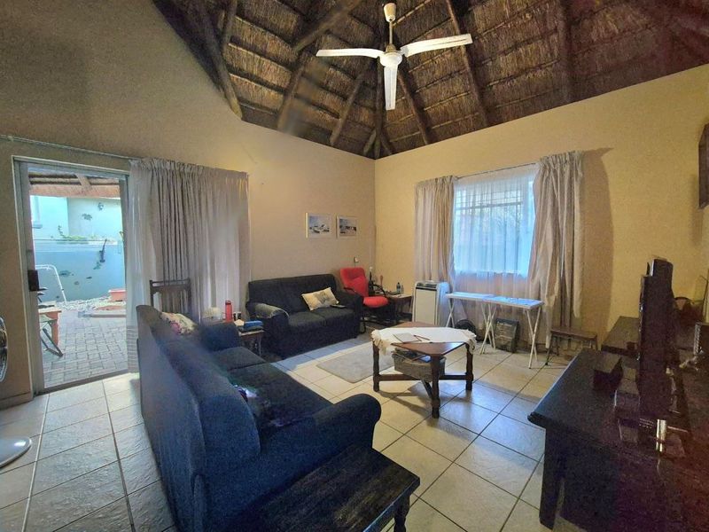 Spacious living room featuring a high vaulted thatched ceiling, ceiling fan, tiled flooring, and direct access to an outdoor patio area.