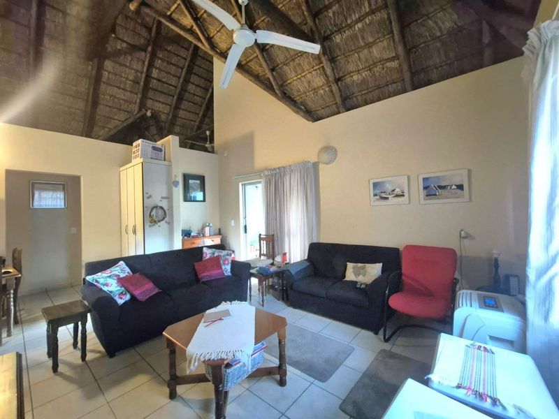 Spacious living area featuring a high vaulted thatched ceiling with exposed timber rafters, ceiling fan, and neutral tiled flooring.