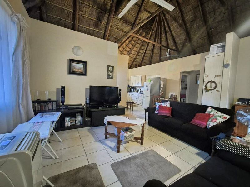 Open-plan living area featuring a high vaulted thatched ceiling with exposed rafters, tiled flooring, and an adjoining kitchen space.
