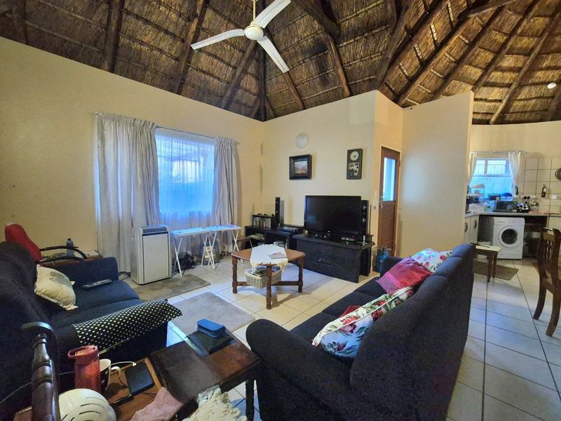 Open-plan living area featuring a high thatched ceiling with exposed rafters, tiled flooring, and an adjoining kitchen space.