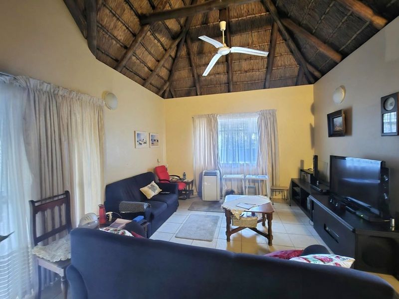 A living room featuring a high vaulted thatched ceiling with exposed timber rafters, tiled flooring, and access to an outdoor area via sliding glass doors.