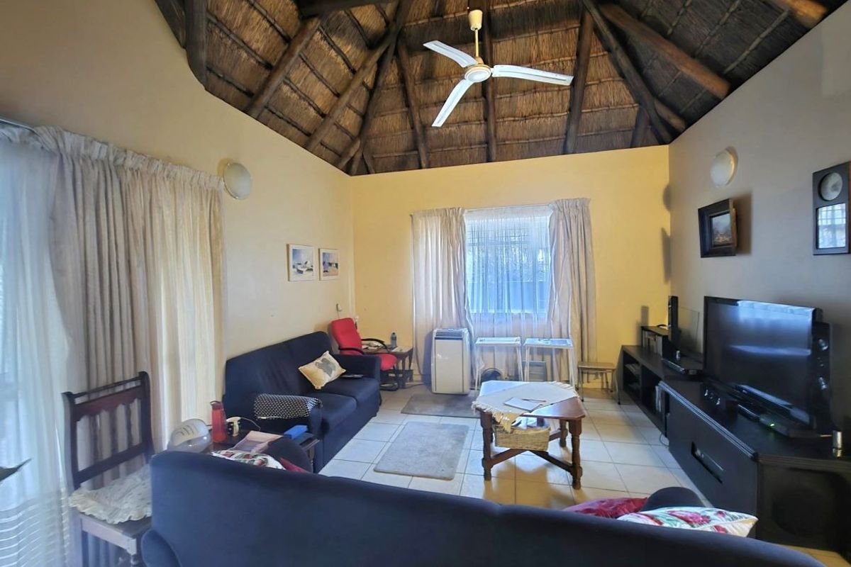 A living room featuring a high vaulted thatched ceiling with exposed timber rafters, tiled flooring, and access to an outdoor area via sliding glass doors.