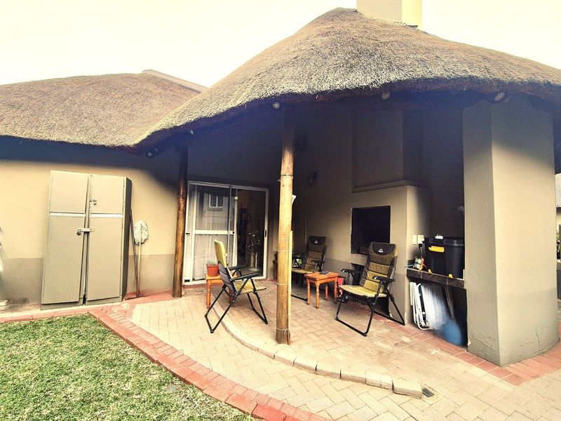 Covered patio area featuring a traditional thatched roof, built-in braai, and brick paved flooring, providing a functional outdoor entertainment space.