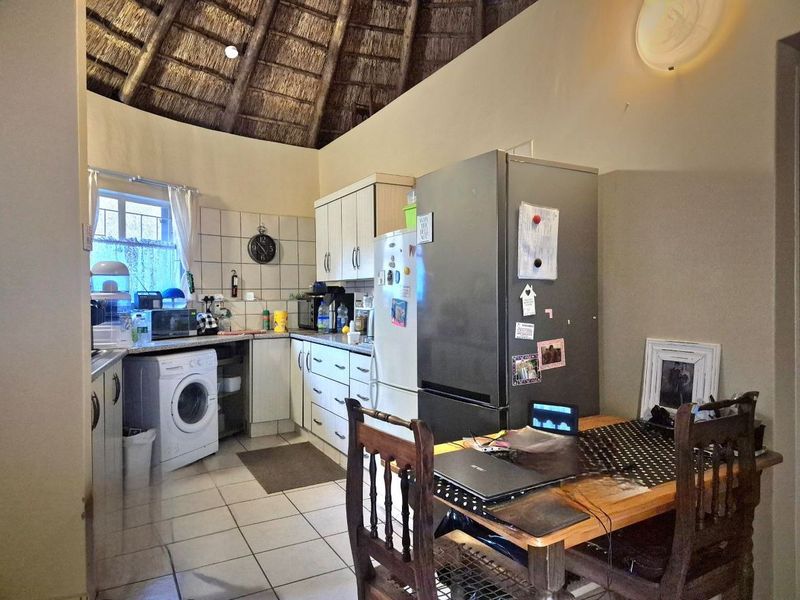 A functional kitchen area featuring a unique thatched ceiling, tiled flooring, and built-in cabinetry with integrated laundry facilities.