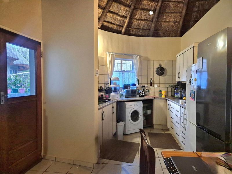 A functional kitchen featuring built-in cabinetry, tiled backsplash, and a unique vaulted thatch roof ceiling, with direct access to the exterior.