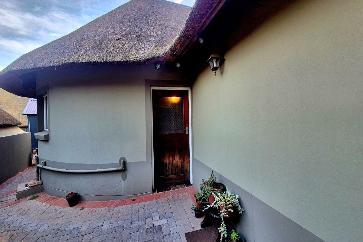 A rear exterior view of a retirement unit featuring a traditional thatch roof, paved patio area, and a timber entrance door.