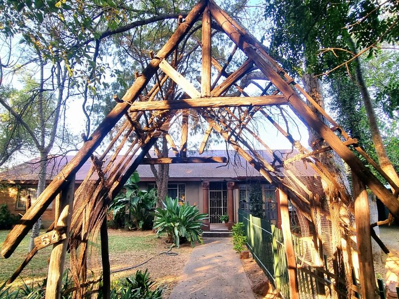 Front view of the property featuring a weathered wooden pergola entrance, paved walkway, and established garden leading to the main house entrance.