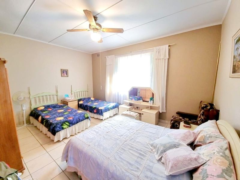 Spacious bedroom featuring tiled flooring, a ceiling fan, and large windows with curtain rails, offering a functional layout.