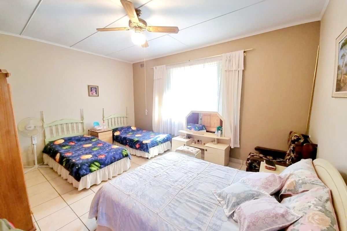Spacious bedroom featuring tiled flooring, a ceiling fan, and large windows with curtain rails, offering a functional layout.